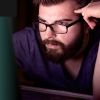 Man with glasses thinking while staring at screen
