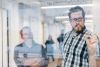 Man in glasses writing on a glass wall with a whiteboard marker