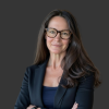Stacey standing with arms crossed, she has long brown hair and is wearing dark framed eyeglasses